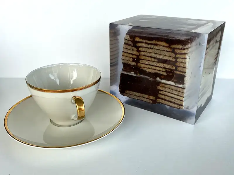 Ein Kuchenstück in einem Kunstharzblock arrangiert mit einer Teetasse